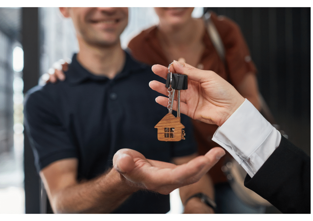 Gros plan sur une main remettant un trousseau de clés de maison, attaché à un porte-clés en forme de maison en bois, à un jeune homme souriant, symbolisant la transmission d'un bien immobilier ou d'un héritage aux héritiers.