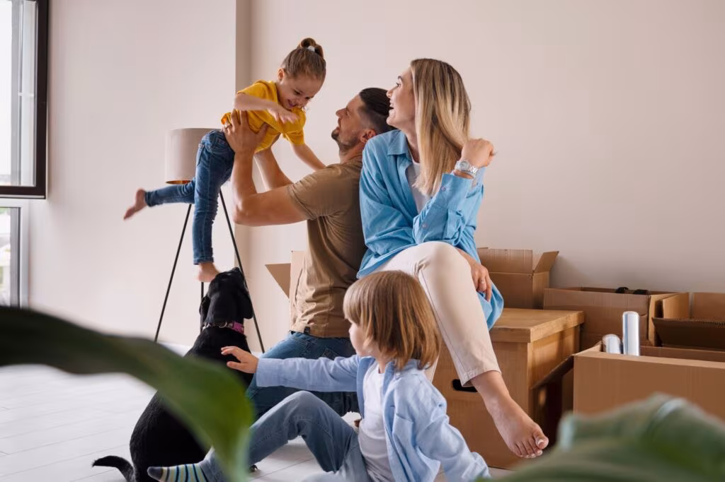 Une famille souriante avec deux enfants et un chien dans un salon lumineux rempli de cartons de déménagement, symbolisant la réussite d'une transmission de patrimoine et l'acquisition d'un nouveau logement grâce aux exonérations de succession.
